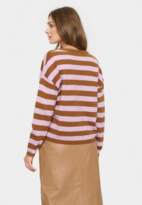 Maglione a righe marroni e viola chiaro con un fit rilassato, scollatura rotonda e maniche lunghe, abbinato a una gonna in pelle beige.