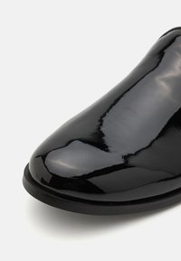 Melnas lakotas ādas kurpes ar gludu, spīguļojošu virsmu, noapaļotu purngalu un šauru, elegantu siluetu. Melnais zole piešķir kontrastu.