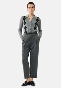 Cardigan gris avec un motif noir et en diamant, boutonné, associé à un pantalon gris taille haute et des mocassins noirs brillants.