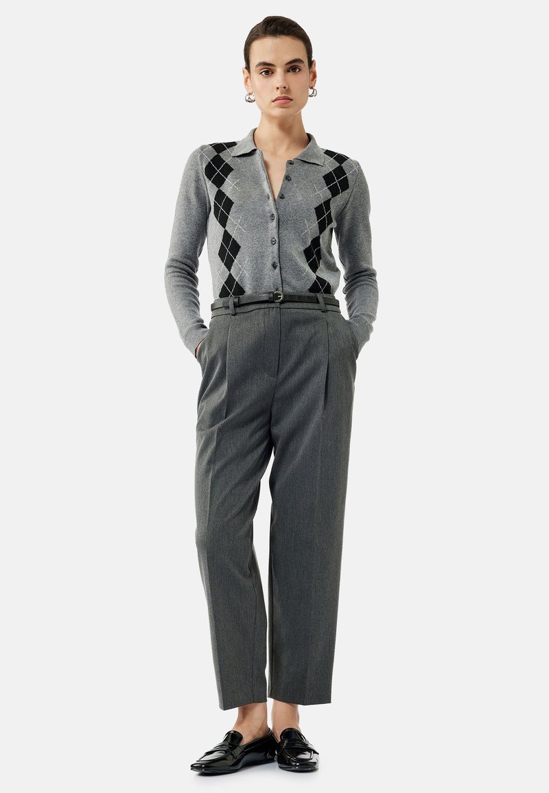 Cardigan gris avec un motif noir et en diamant, boutonné, associé à un pantalon gris taille haute et des mocassins noirs brillants.