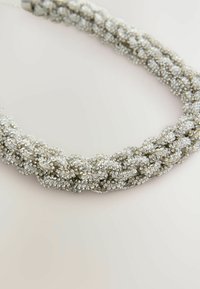 Pītā kaklarota, kas izgatavota no sudraba tonētiem pērlēm, ar fakturētu virsmu un mirdzošiem akcentiem visā dizainā.