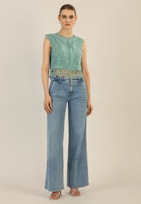 Ein mintgrünes Spitzencrop-Top mit gewellten Rändern, kombiniert mit hochtaillierten, weiten hellblauen Jeans und silbernen Sandalen.