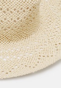 Sombrero de paja beige de ala ancha con una textura tejida, que presenta patrones abiertos y un diseño suave y flexible, adecuado para un uso casual.
