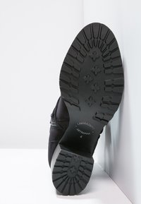 Botte en daim noir avec une semelle en caoutchouc texturée, présentant un motif de semelle et des détails en relief sur le talon.