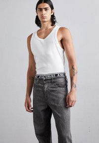 Top alb din bumbac cu decupaje largi pentru brațe, asortat cu blugi gri. Blugii au o talie neagră cu logo-ul "Versace Jeans". Textură subtilă pe blugi.