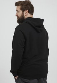 Sudadera con capucha negra de material suave; presenta un corte relajado, mangas largas y un bolsillo canguro.