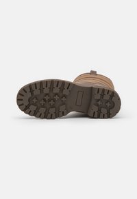 Botte en caoutchouc marron avec semelle texturée, présentant des crampons profonds pour une traction optimale et une languette à l'arrière pour un enfilage facile.