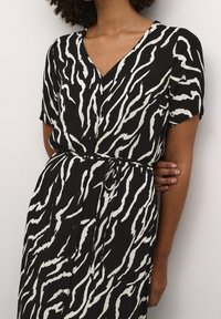 Robe chemise à manches courtes avec imprimé zèbre noir et blanc, col en V, boutons et ceinture nouée à la taille. Tissu léger avec un design fluide.