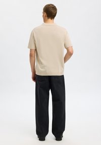 Polo shirt beige à manches courtes avec un col classique, associé à un jean noir ample. Texture de tissu lisse et détails minimalistes.