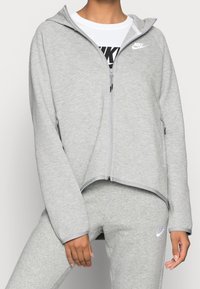 Grå huva sweatshirt med dragkedja framtill, tillverkad av mjukt tyg. Har en logotyp på bröstet och ribbade manschetter. Avslappnad, ledig passform.