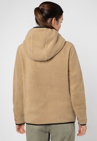 Beige Fleecejacke mit Kapuze, strukturiertem Stoff und schwarzem Besatz an Saum und Bündchen. Die Rückansicht zeigt einen gemütlichen, lockeren Schnitt.