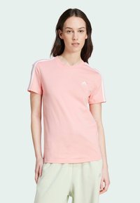 T-shirt em algodão rosa com mangas curtas, apresentando riscas laterais brancas e um pequeno logótipo branco no lado esquerdo do peito. Textura suave.