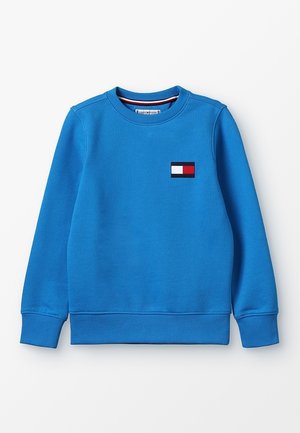 Blauwe katoenen trui met lange mouwen, geribbelde manchetten en een ronde hals. Voorzien van een klein logo met rode, witte en blauwe elementen.