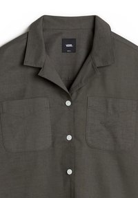 Chemise gris à boutons avec un tissu léger, deux poches poitrine et un petit logo brodé. Dotée d'un col de style camp et de boutons blancs.