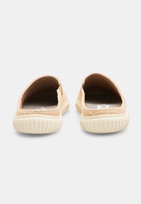 Beige slip-on kengät, joissa on teksturoitu päällinen, joustavat sivut ja off-white kumipohja, jossa on urat. Auki takana helpottamaan pukemista.