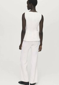 Top peplo bianco senza maniche abbinato a pantaloni bianchi su misura. Tessuto liscio con una silhouette aderente. Calzature nere completano il look.