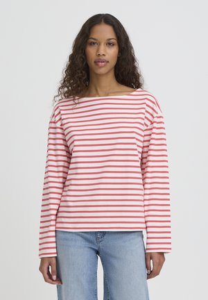 Haut à manches longues blanc avec des rayures horizontales rouges. Il comporte un col large et une coupe décontractée. Associé à un jean en denim bleu clair.