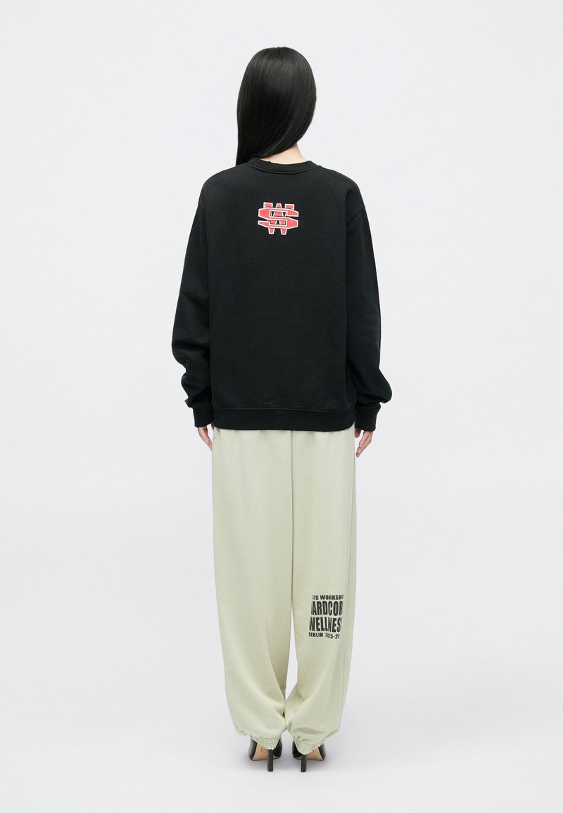 Zwarte sweatshirt met rood logo op de rug, gecombineerd met lichtgroene wijde broek met een grafische print. Soepele stof, relaxte fit.