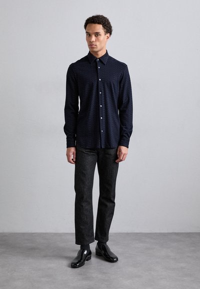 Camicia button-up blu scuro con un motivo sottile, maniche lunghe e colletto. Abbinata a pantaloni in denim scuri e scarpe nere lucide.