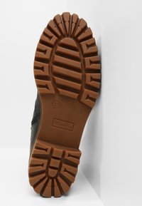 Semelle d'une chaussure noire avec des crampons épais et profonds de couleur fauve, conçus pour l'adhérence, indiquant la pointure 37 et la marque Tamaris.