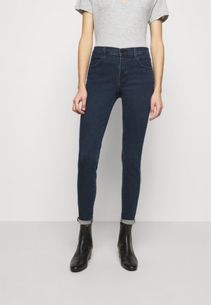 Jeans ajustados de mezclilla de color azul oscuro con una cintura alta, cinco bolsillos y dobladillo enrollado. Combinados con una camiseta gris de manga corta y botas negras hasta el tobillo.