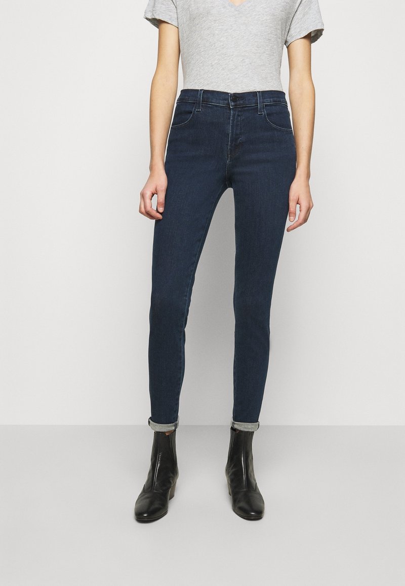 Jeans ajustados de mezclilla de color azul oscuro con una cintura alta, cinco bolsillos y dobladillo enrollado. Combinados con una camiseta gris de manga corta y botas negras hasta el tobillo.
