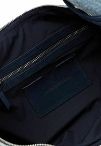 Interno blu navy di una borsa con una tasca con zip e un portacarte in pelle testurizzata etichettato "VISIONARES." Una morbida fodera in tessuto avvolge l'interno.
