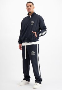 Marine trainingspak gemaakt van zachte stof, met witte zijstrepen, een ritsjack met zakken en bijpassende broeken met een logo.