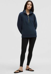 Navy zip-up sweatshirt with a high collar and front pocket, paired with black leggings and flip-flops. Soft fabric with relaxed fit.