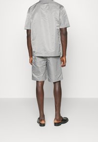 Grå kortärmad skjorta och matchande shorts i ett mjukt, lätt tyg. Skjortan har en enkel krage; shorts har en avslappnad passform.