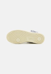 Nike sneakersåle i beige gummi med sirkulære mønstre og en sentral spor. Har en glatt tekstur og logodetalj.