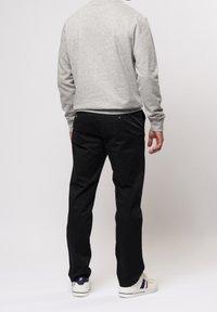 Grauer Pullover mit langen Ärmeln, kombiniert mit schwarzer Hose. Das Outfit wird durch weiße Sneakers mit farbigen Akzenten vervollständigt.