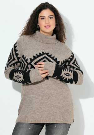 Suéter oversized beige con patrones geométricos negros en las mangas, cuello alto acanalado y aberturas laterales. Textura suave, mangas largas, ajuste relajado.