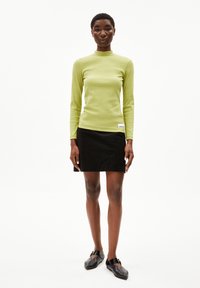Langsleeve, geribbelde, limoen groene top gecombineerd met een zwarte rok. De outfit heeft een gestructureerde afwerking en een klein label aan de zoom.