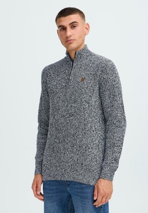Marineblå og hvid mønstret sweater med en kvart-zip krave og et lille brunt logo. Blød strikstruktur med lange ærmer og en tætsiddende pasform.