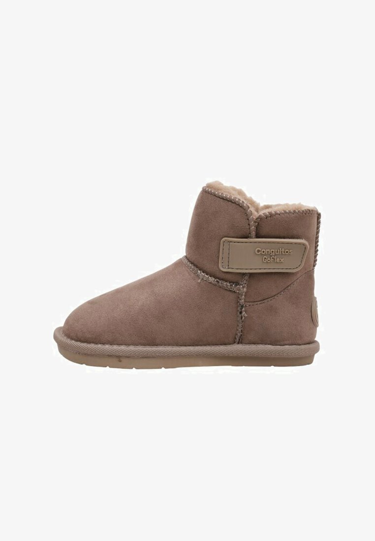 Botín de ante marrón con un suave forro de forro polar, una correa lateral con el nombre de la marca y una suela de goma plana.