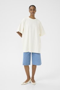 Overmaat crèmekleurig T-shirt met korte mouwen, gecombineerd met lichte spijkerbroekshorts tot de knie en witte puntige hakken. Eenvoudig en minimalistisch ontwerp.