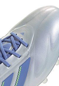 Light grey soccer cleat with textured synthetic upper, blue laces, blue and green accents, and distinct traction studs on the sole.