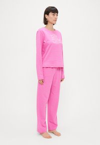 Ružový pruhovaný pyžamový set z mäkkého materiálu. Dlhý rukáv s logom, zodpovedajúce nohavice s elastickým pásom. Pohodlný a voľný strih.