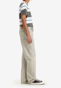 Randig t-shirt i grått, vitt och blått, ihop med ljusgrå raka jeans och svarta sneakers med vita sulor.