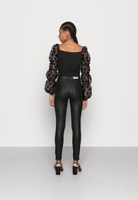 Top negro con mangas abullonadas y transparentes con lunares negros, combinado con pantalones ajustados negros y sandalias de tacón bloque con tiras.