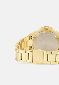 Montre-bracelet en or avec un bracelet en métal ; dotée d'un boîtier rond et de maillons texturés. Comprend une couronne et un logo en relief sur le fermoir.