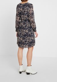 Floral print dress in navy, featuring long sleeves and a cinched waist. Paired with white ankle boots. Lightweight, sheer fabric.