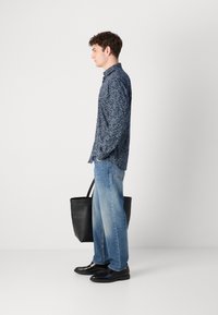 Navy button-up shirt with a small white floral pattern, paired with light blue jeans and black leather shoes, carrying a black tote bag.