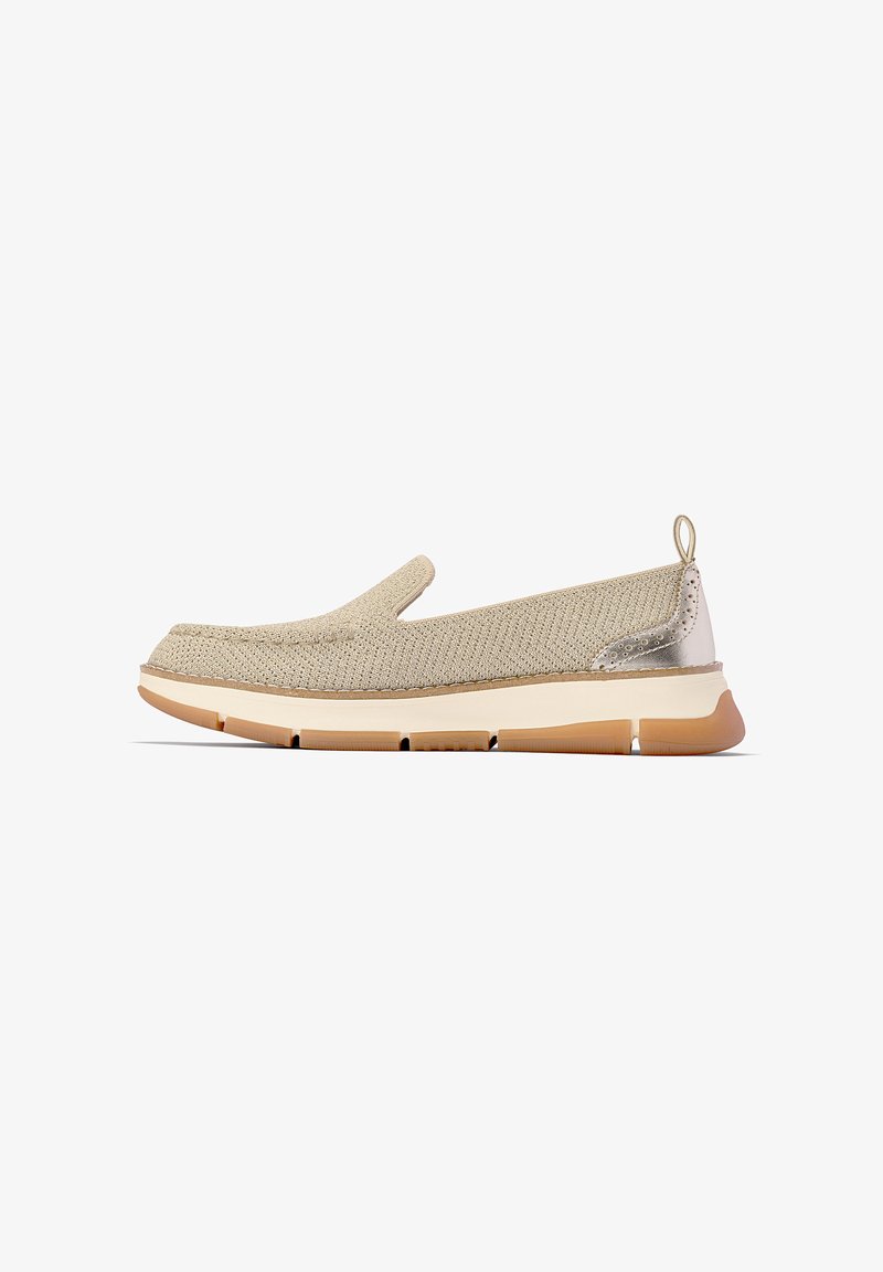 Beige slip-on sko med en texturerad stickad ovandel, en metallisk detalj vid hälkappan och en flexibel, ljusfärgad sula med greppfunktioner.