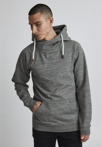 Sudadera gris con cuello tipo embudo, cierre con cordón y bolsillo canguro. La tela parece suave y texturizada, con puños y dobladillo acanalados.