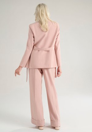 Completo su misura rosa chiaro composto da una giacca con cintura e pantaloni a gamba larga, entrambi con sottili dettagli di texture.