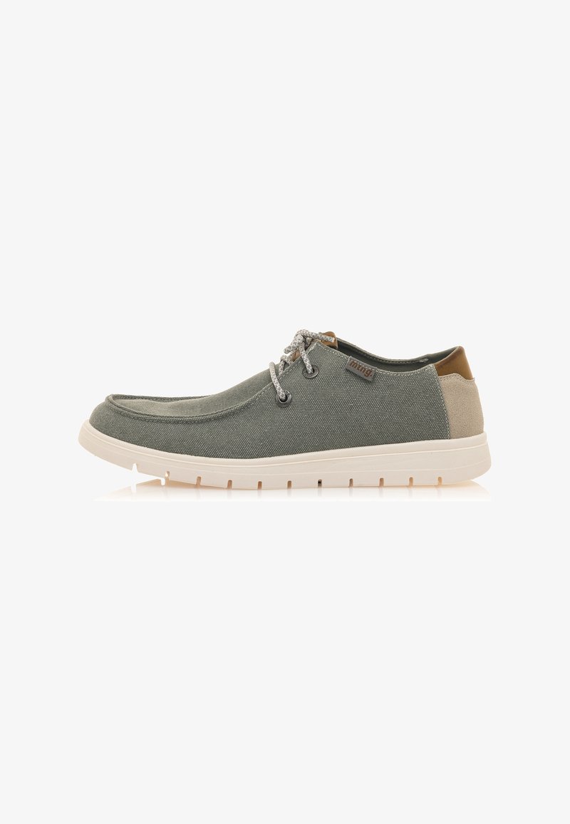 Zapatillas de lona gris con punta redondeada, parte superior texturizada, acento en el talón en color tostado y diseño de cordones. Suela de goma con pequeños recortes.