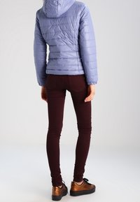 Ljuslila tygjacka med huva, kombinerad med mörk burgundyröda skinny jeans och bruna plattformsskor. Slät textur, figurnära design.