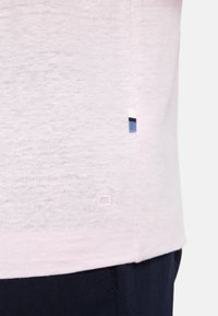 Lichtroze katoenen shirt met korte mouwen en een subtiele heather textuur. Heeft een klein blauw-wit label aan de zoom en minimale merktekens.